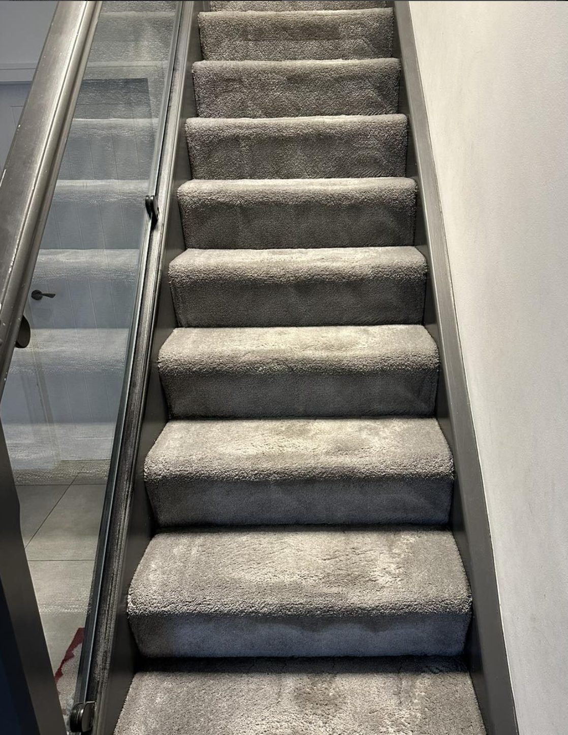 Modern staircase carpet beside a glass balustrade